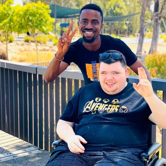 NDIS participant in wheelchair with support worker smiling outdoors - NDIS Travel assistance