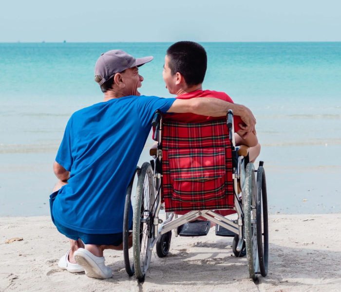 NDIS participant in wheelchair enjoying the beach with a caregiver