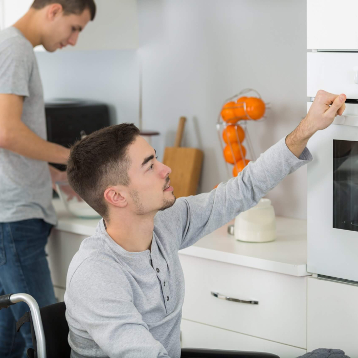 Assistance with Daily Life - Young man in wheelchair using kitchen oven