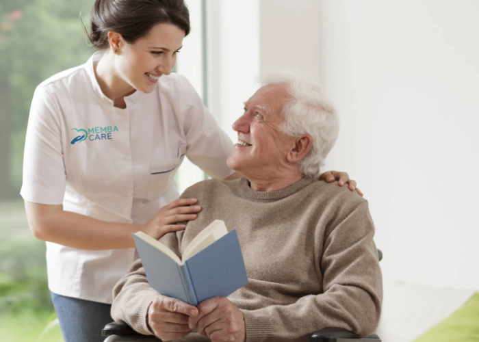 Caregiver assisting elderly man in wheelchair with reading a book
